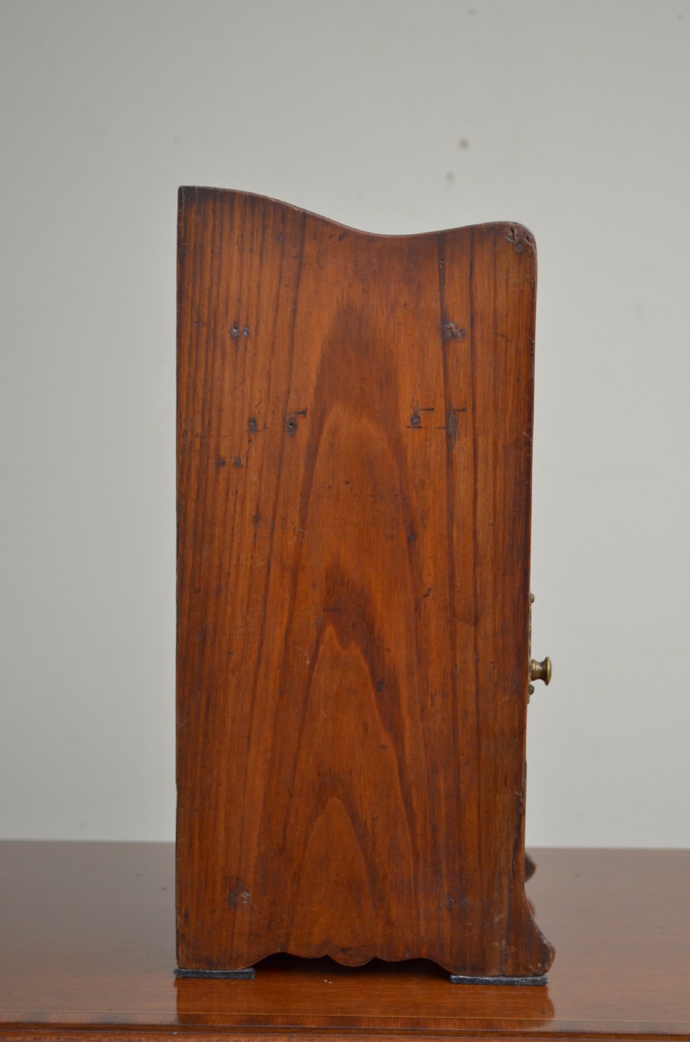 An Arts and Crafts oak smokers cabinet featuring a single glazed door, decorative brass handles, and a shaped top gallery with a central circular cutout. View V