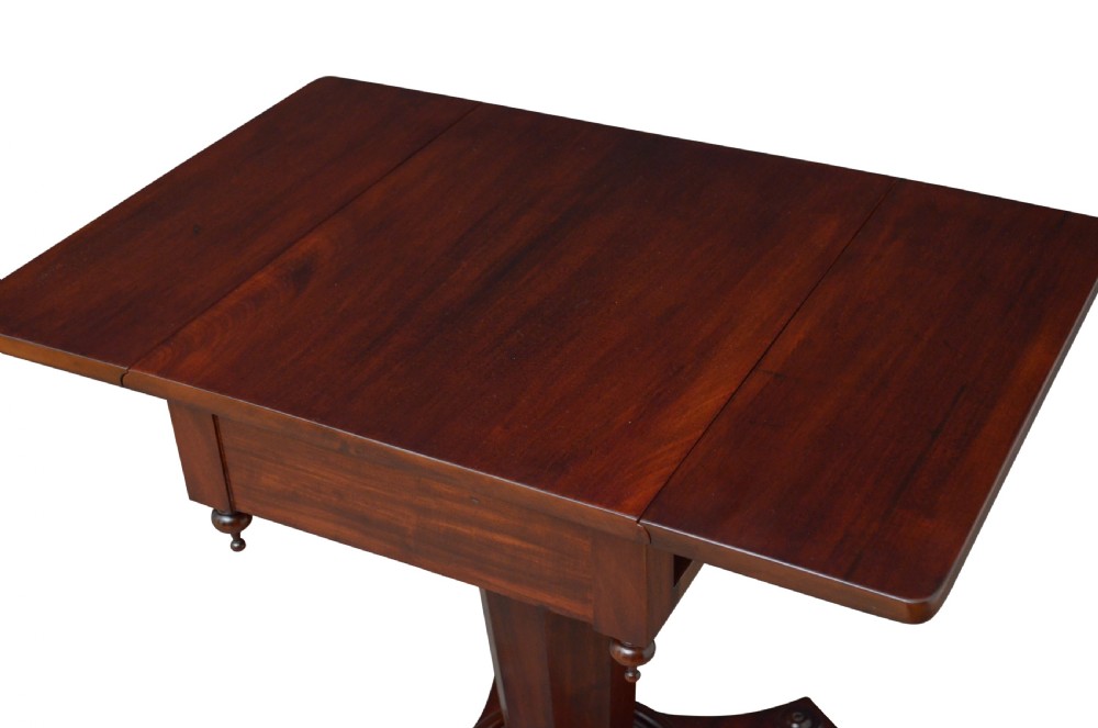 An antique William IV mahogany drop-leaf table featuring a rectangular top with hinged side flaps, supported by a central column stem and a quadform plinth base on bun feet. View IV
