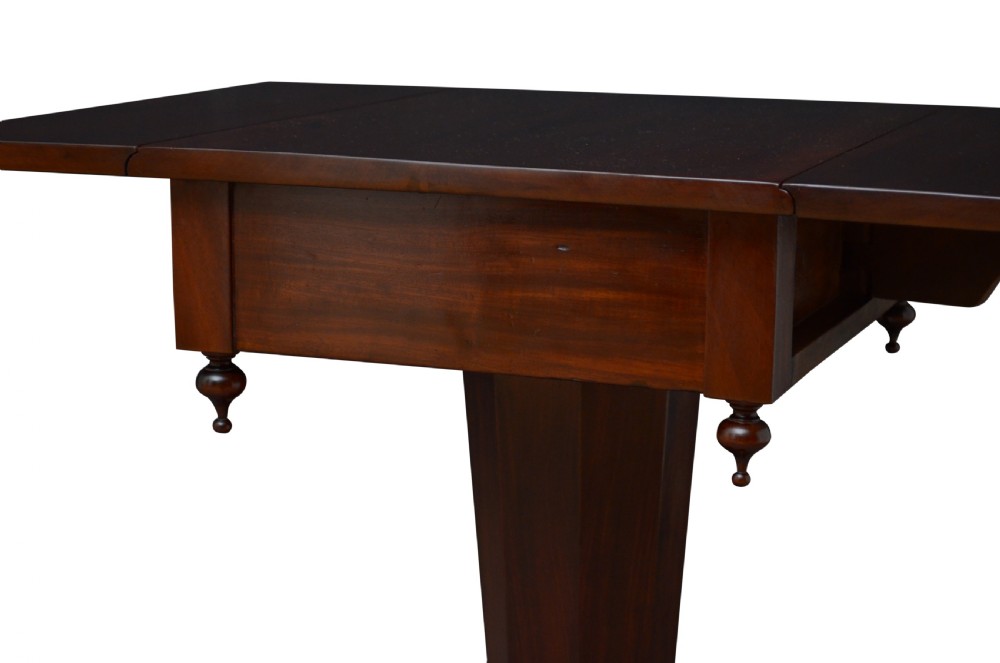 An antique William IV mahogany drop-leaf table featuring a rectangular top with hinged side flaps, supported by a central column stem and a quadform plinth base on bun feet. View VI