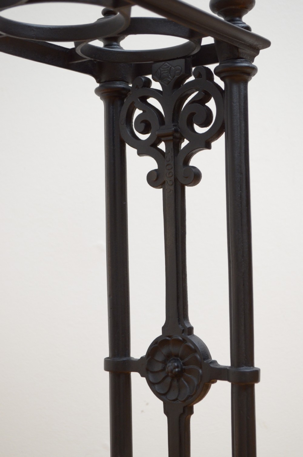 An ornate black cast iron umbrella and walking stick stand featuring openwork scroll panels, vertical pillars, and a compartmentalised base drip tray. View II