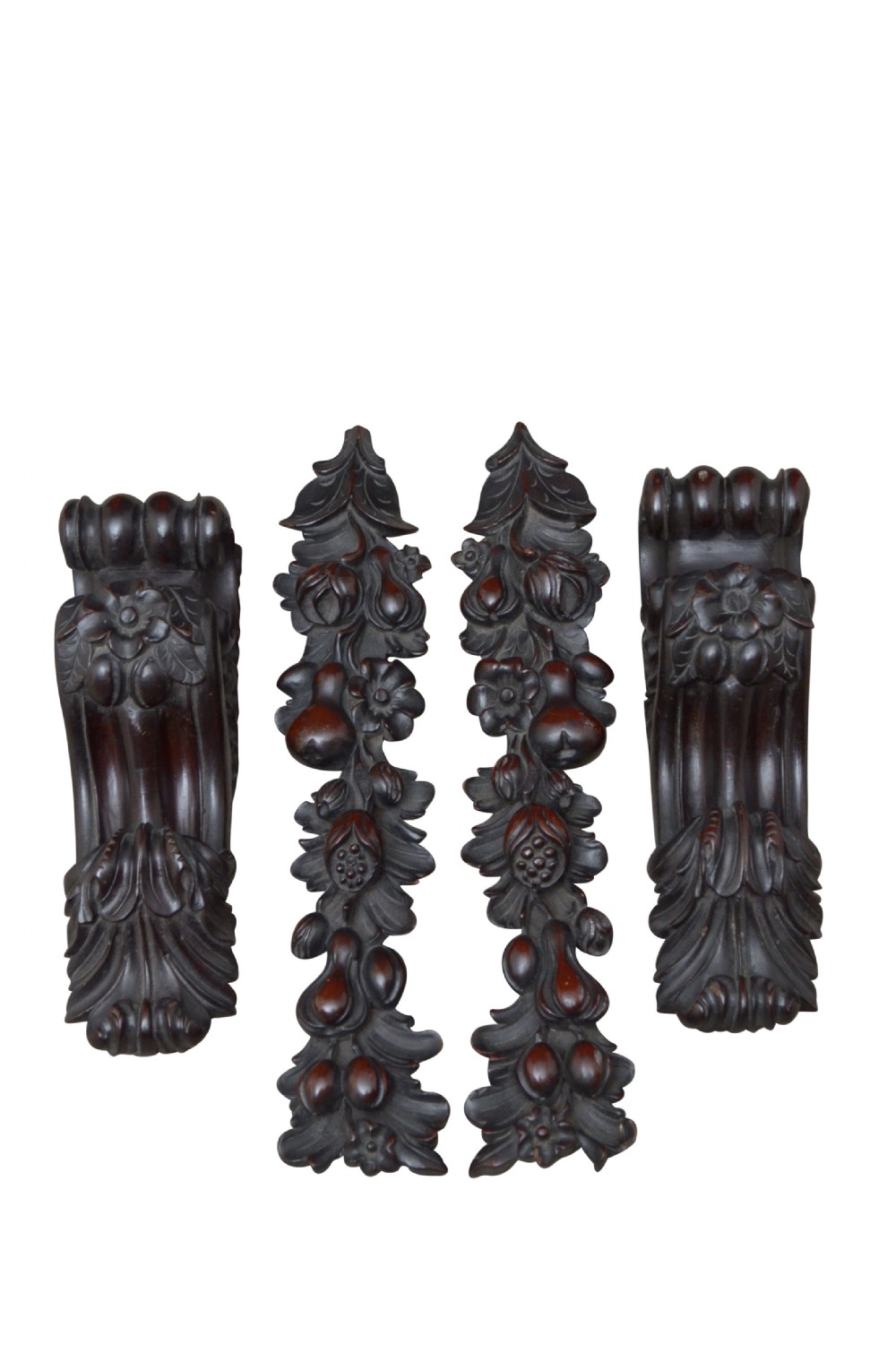 Four dark mahogany architectural elements featuring high-relief carvings of fruit and foliage, comprising two curved corbels and two vertical panels.
