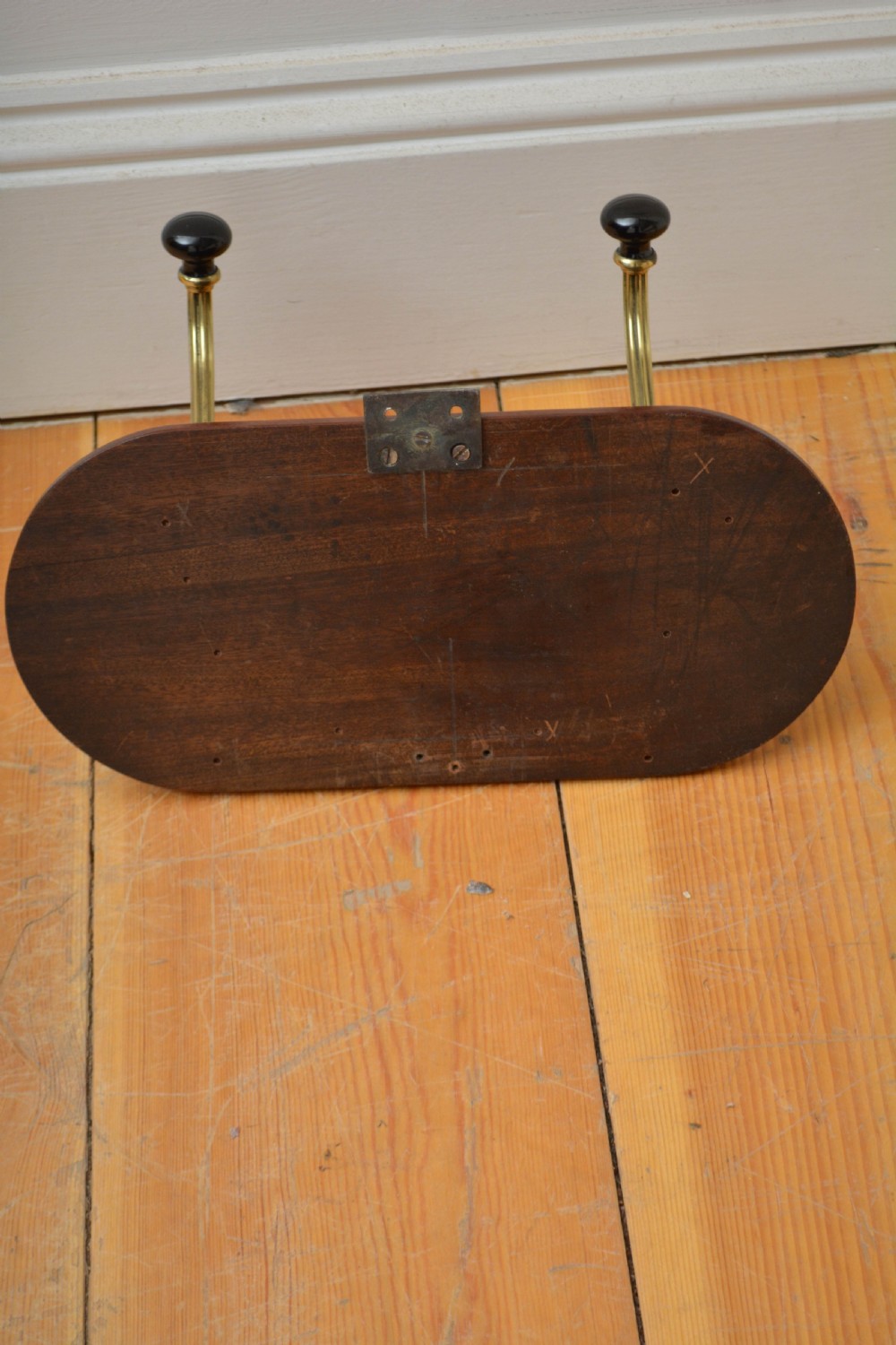 An antique wall-mounted coat rack featuring a polished mahogany backboard fitted with two ornate brass hooks with black ceramic finials. View VIII
