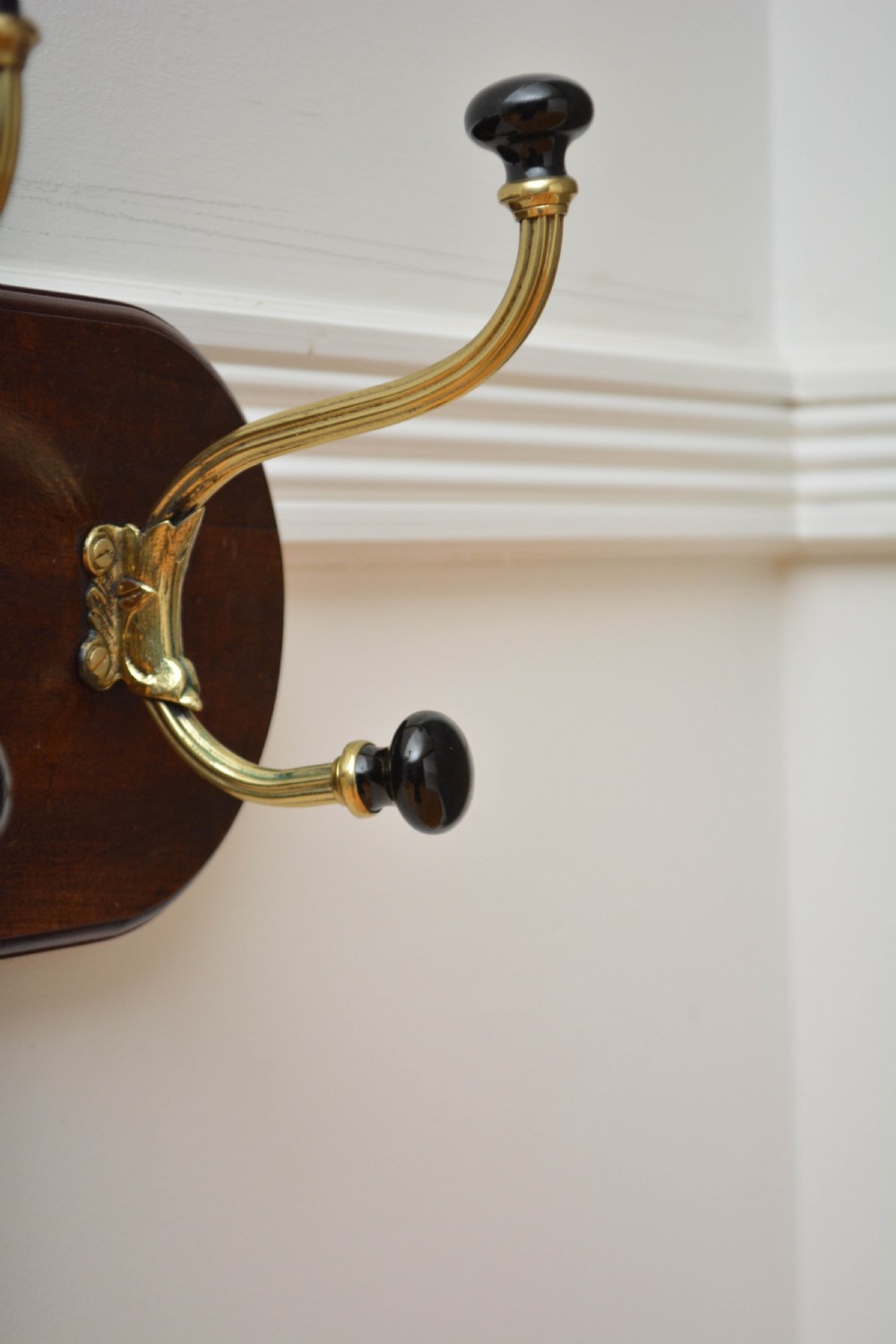 An antique wall-mounted coat rack featuring a polished mahogany backboard fitted with two ornate brass hooks with black ceramic finials. View X