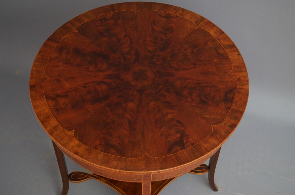 A circular Edwardian occasional table made of polished flame mahogany with inlaid satinwood borders and four slender splayed legs connected by a lower stretcher. View V