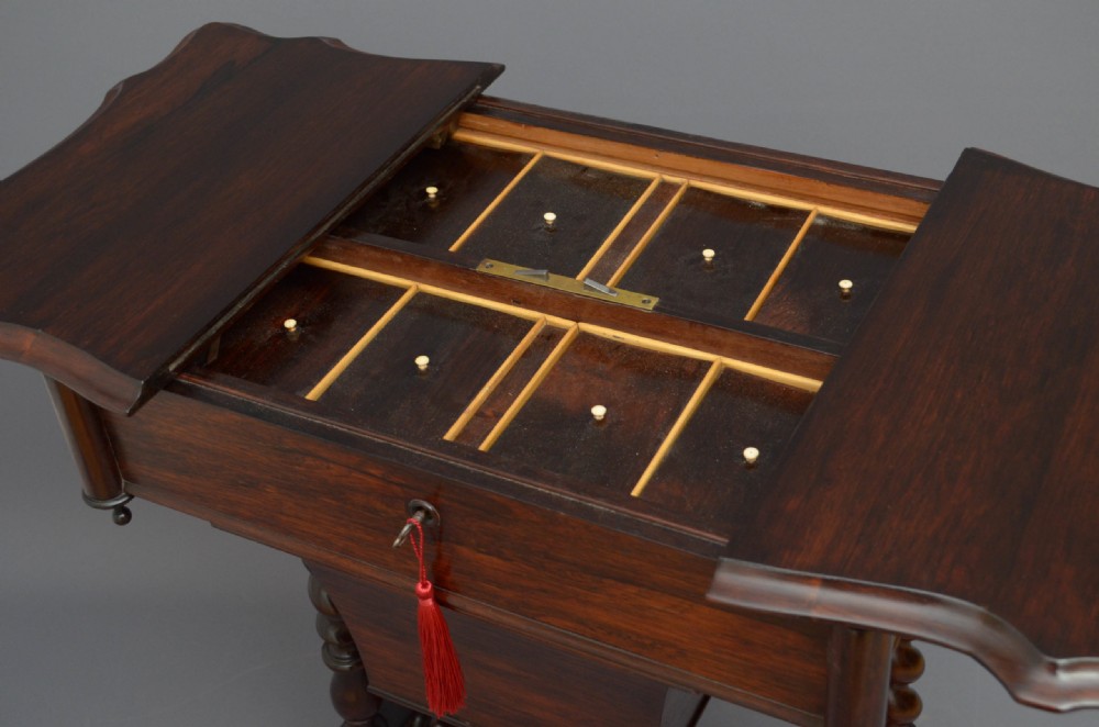A Victorian rosewood work table featuring a hinged top surface, a keyhole drawer, a lower wooden work basket, four barley twist support legs, and scroll feet. View IV