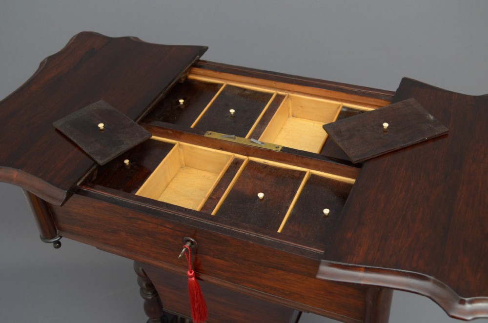 A Victorian rosewood work table featuring a hinged top surface, a keyhole drawer, a lower wooden work basket, four barley twist support legs, and scroll feet. View VII