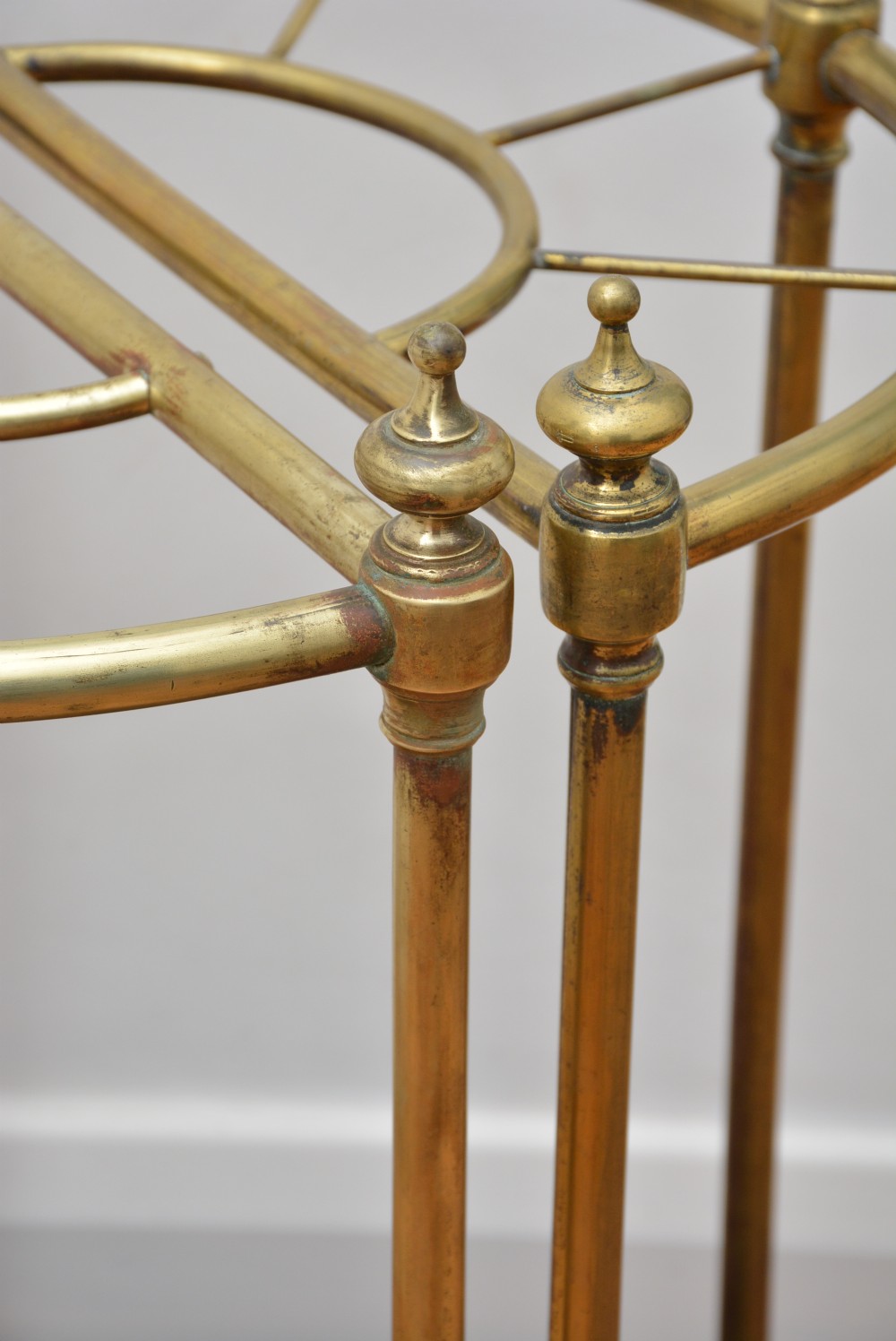 A pair of semi-circular Victorian brass umbrella stands featuring turned finials, internal division rails, and heavy black cast iron drip bases. View II