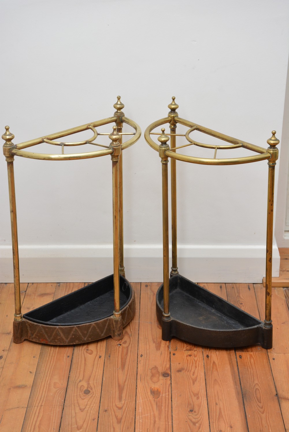 A pair of semi-circular Victorian brass umbrella stands featuring turned finials, internal division rails, and heavy black cast iron drip bases. View III