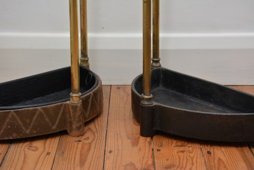 A pair of semi-circular Victorian brass umbrella stands featuring turned finials, internal division rails, and heavy black cast iron drip bases. View IV
