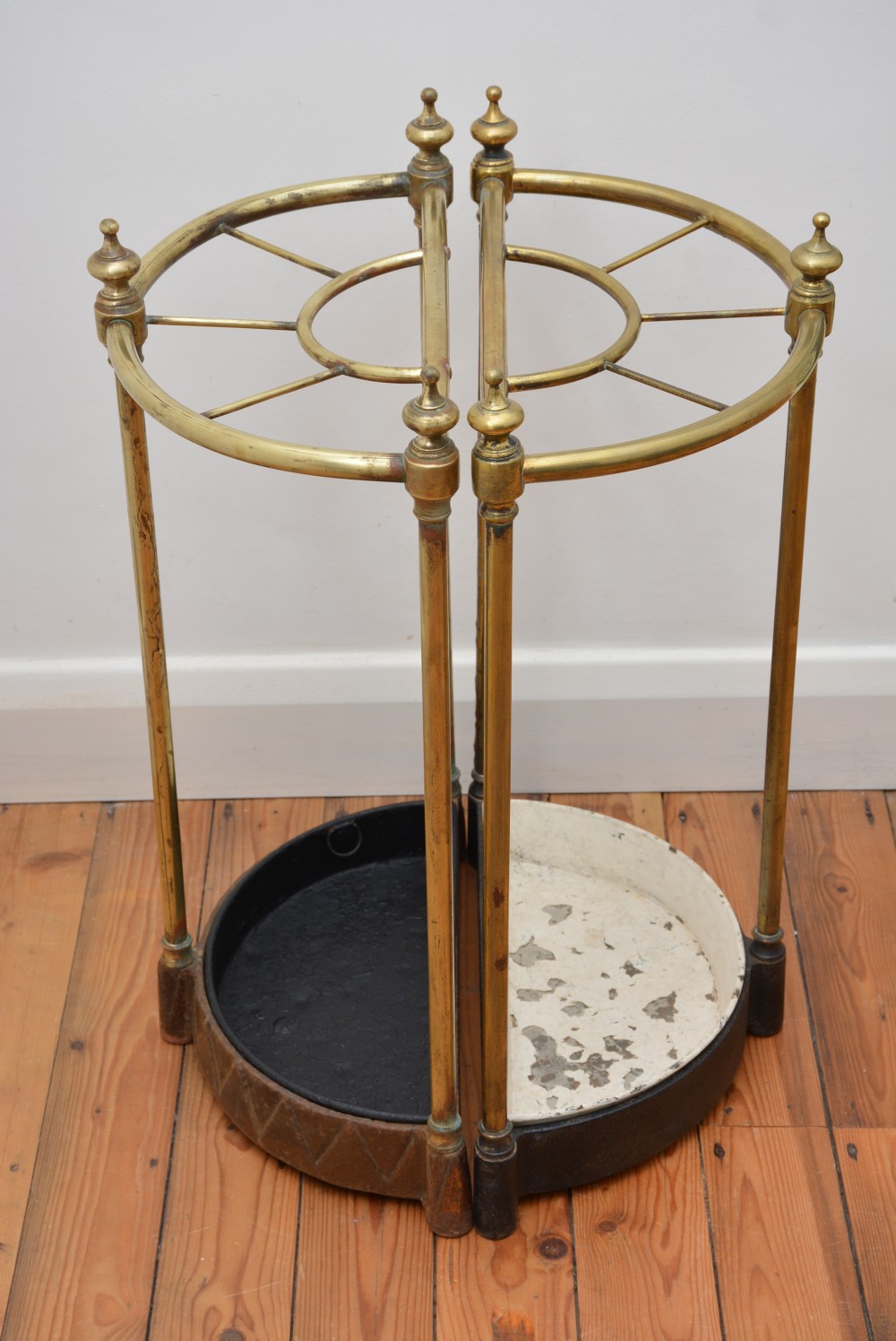 A pair of semi-circular Victorian brass umbrella stands featuring turned finials, internal division rails, and heavy black cast iron drip bases. View V