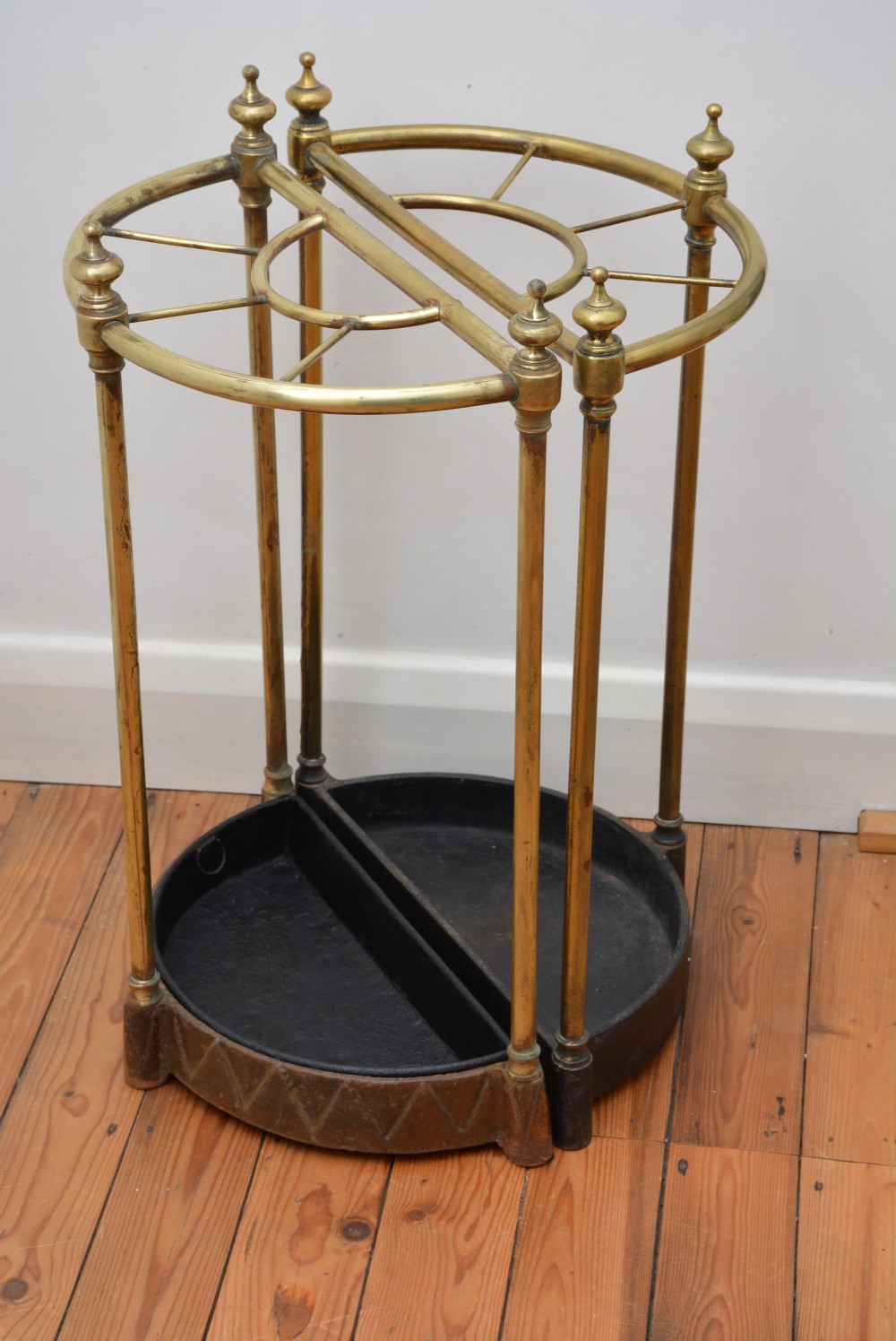 A pair of semi-circular Victorian brass umbrella stands featuring turned finials, internal division rails, and heavy black cast iron drip bases. View VI