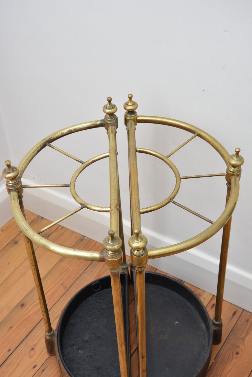 A pair of semi-circular Victorian brass umbrella stands featuring turned finials, internal division rails, and heavy black cast iron drip bases. View VII