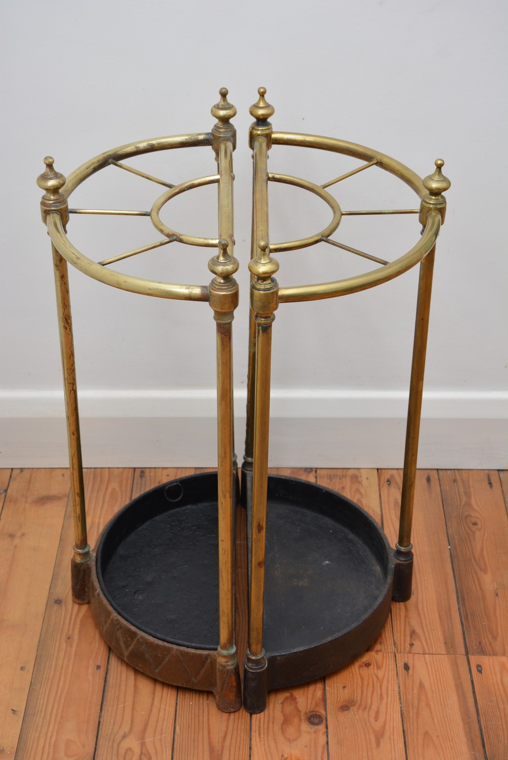 A pair of semi-circular Victorian brass umbrella stands featuring turned finials, internal division rails, and heavy black cast iron drip bases. View IX