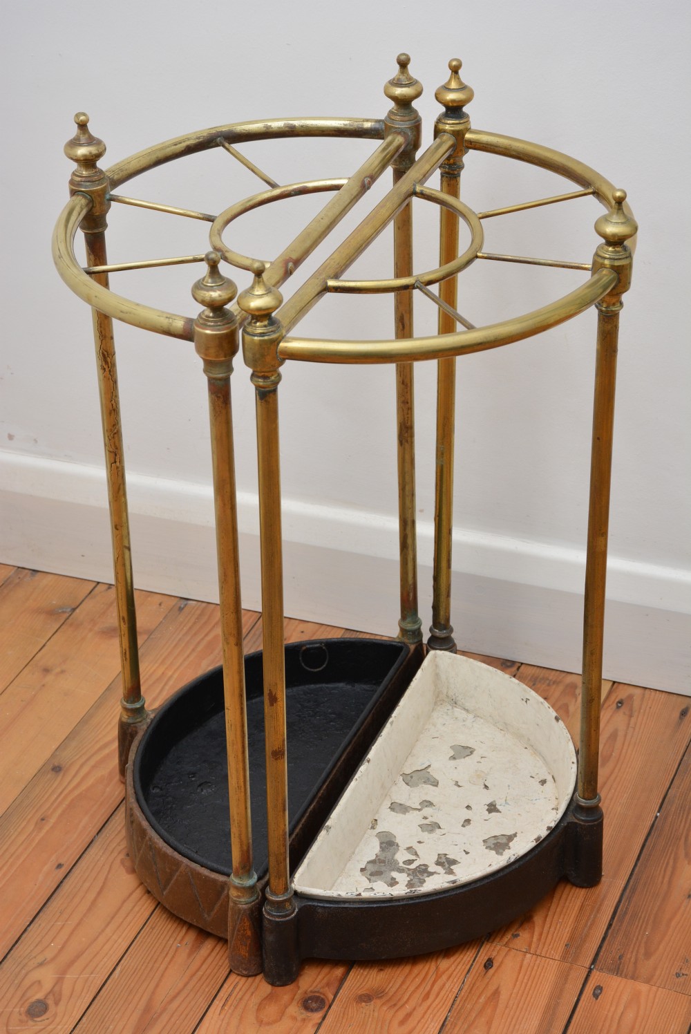 A pair of semi-circular Victorian brass umbrella stands featuring turned finials, internal division rails, and heavy black cast iron drip bases. View X