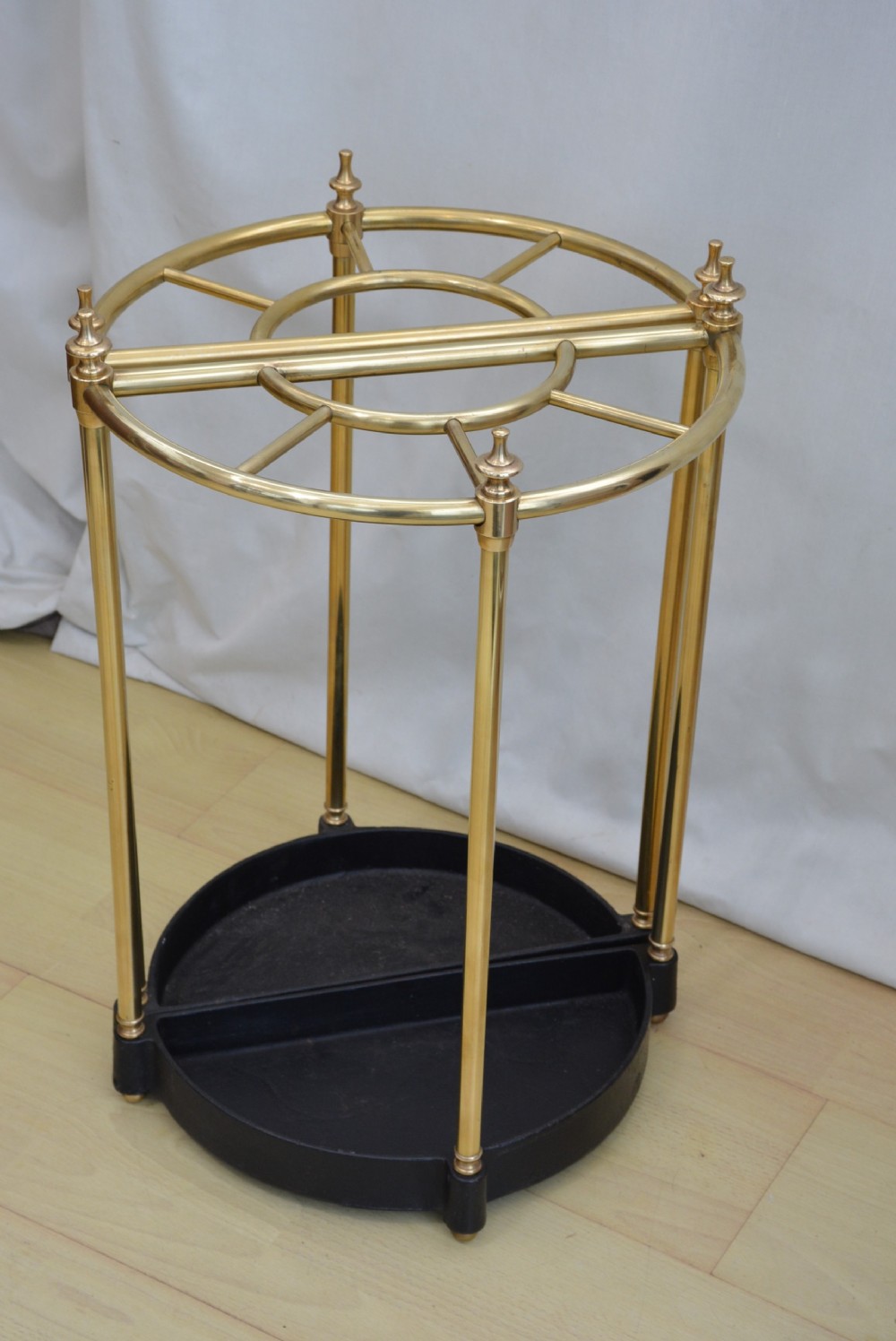A pair of early 20th-century semi-circular brass umbrella stands with finial posts and black cast iron drip trays, placed back to back. View III