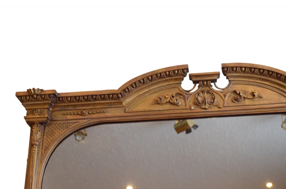 A large rectangular giltwood overmantel mirror featuring an arched top frame, carved cresting, side pilasters, and a gold finish. View X