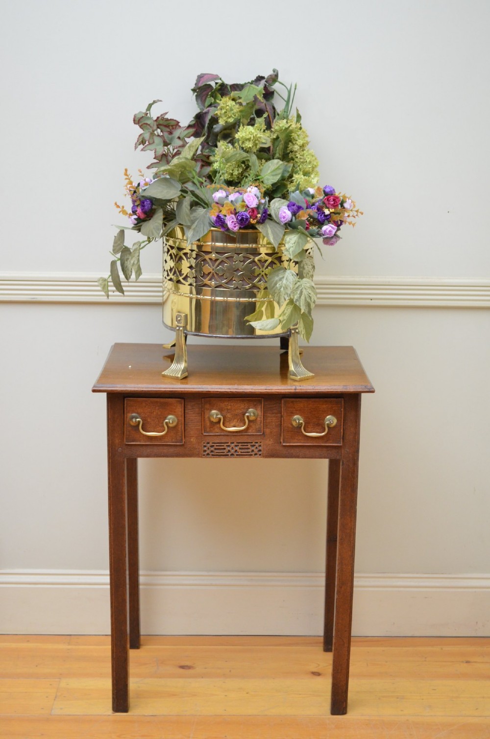 An antique riveted brass coal bin with a curved front, embossed Celtic knot motif, drop ring handles, and ball feet. View III