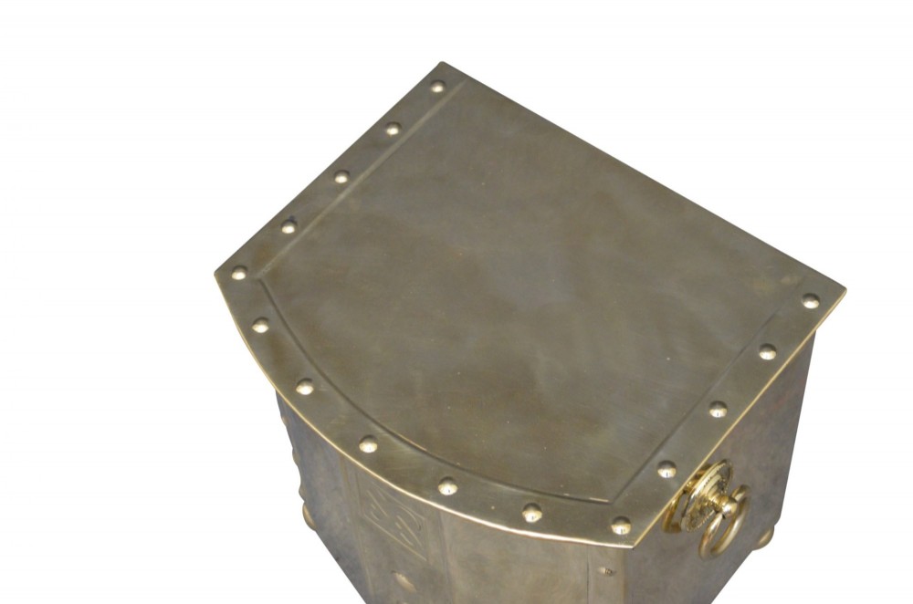 An antique riveted brass coal bin with a curved front, embossed Celtic knot motif, drop ring handles, and ball feet. View VI