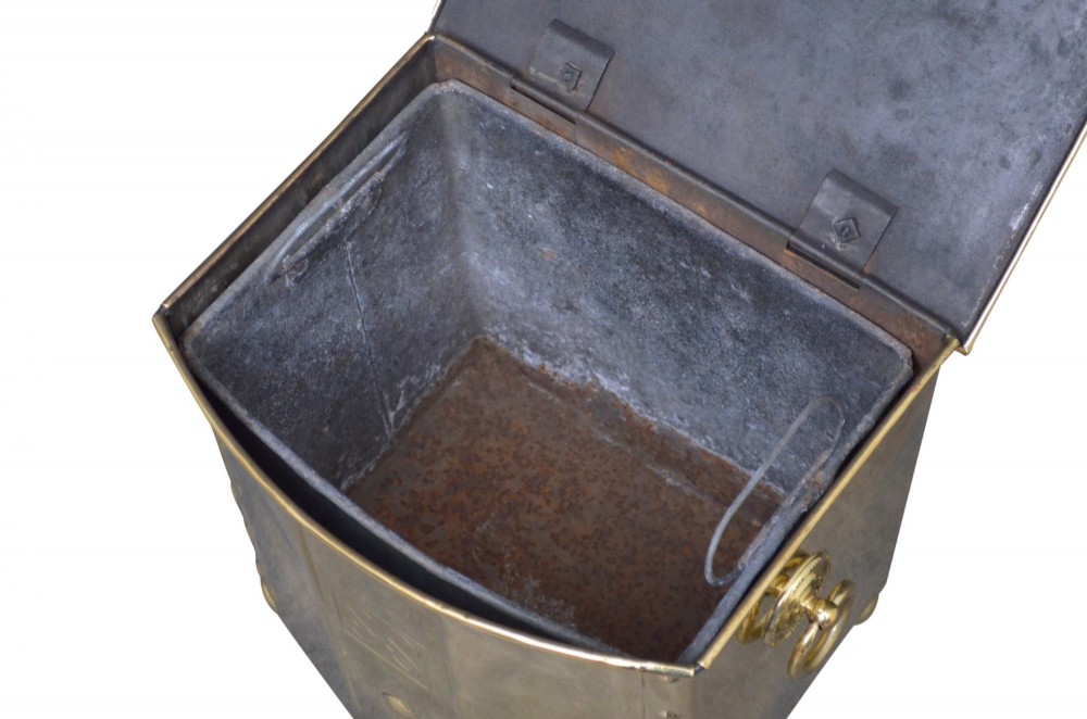 An antique riveted brass coal bin with a curved front, embossed Celtic knot motif, drop ring handles, and ball feet. View X