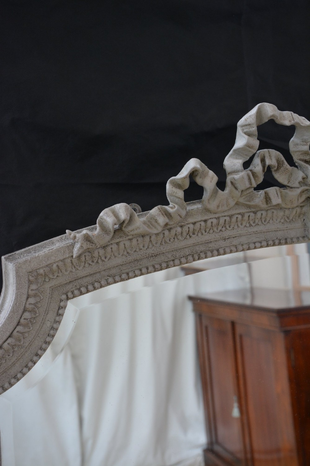 A tall grey-painted French Rococo style wall mirror featuring a carved ribbon top crest and scroll detailing. View IX