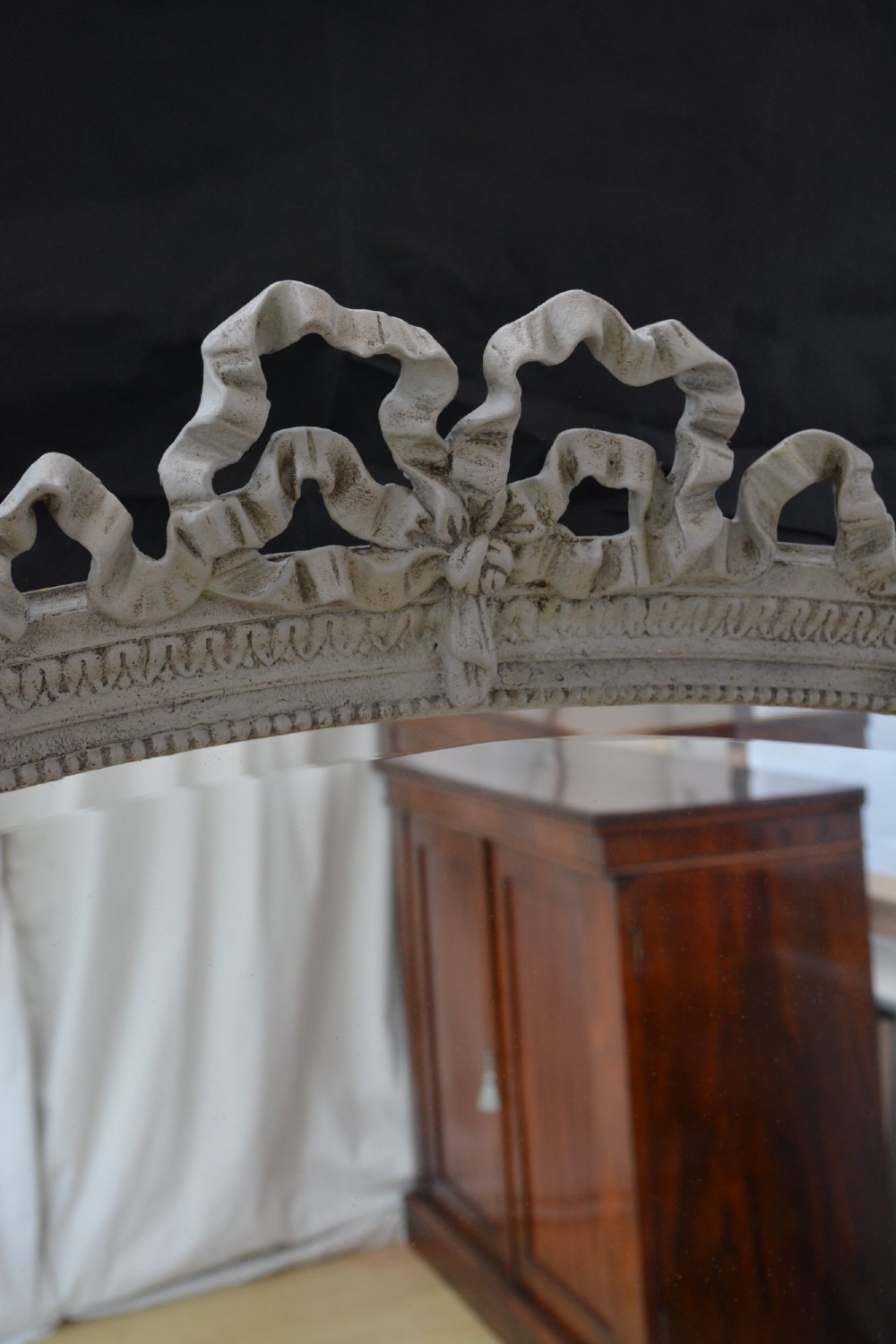 A tall grey-painted French Rococo style wall mirror featuring a carved ribbon top crest and scroll detailing. View X