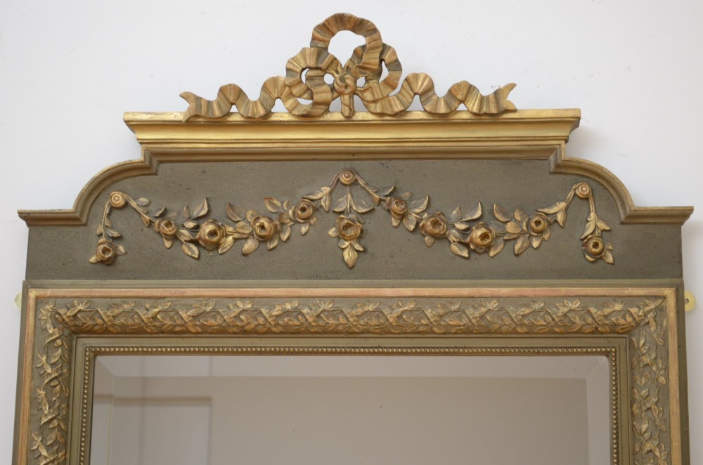 A tall antique French pier mirror featuring a gilded ribbon cresting, carved floral swags, and leaf moulding framing rectangular mirror glass. View II