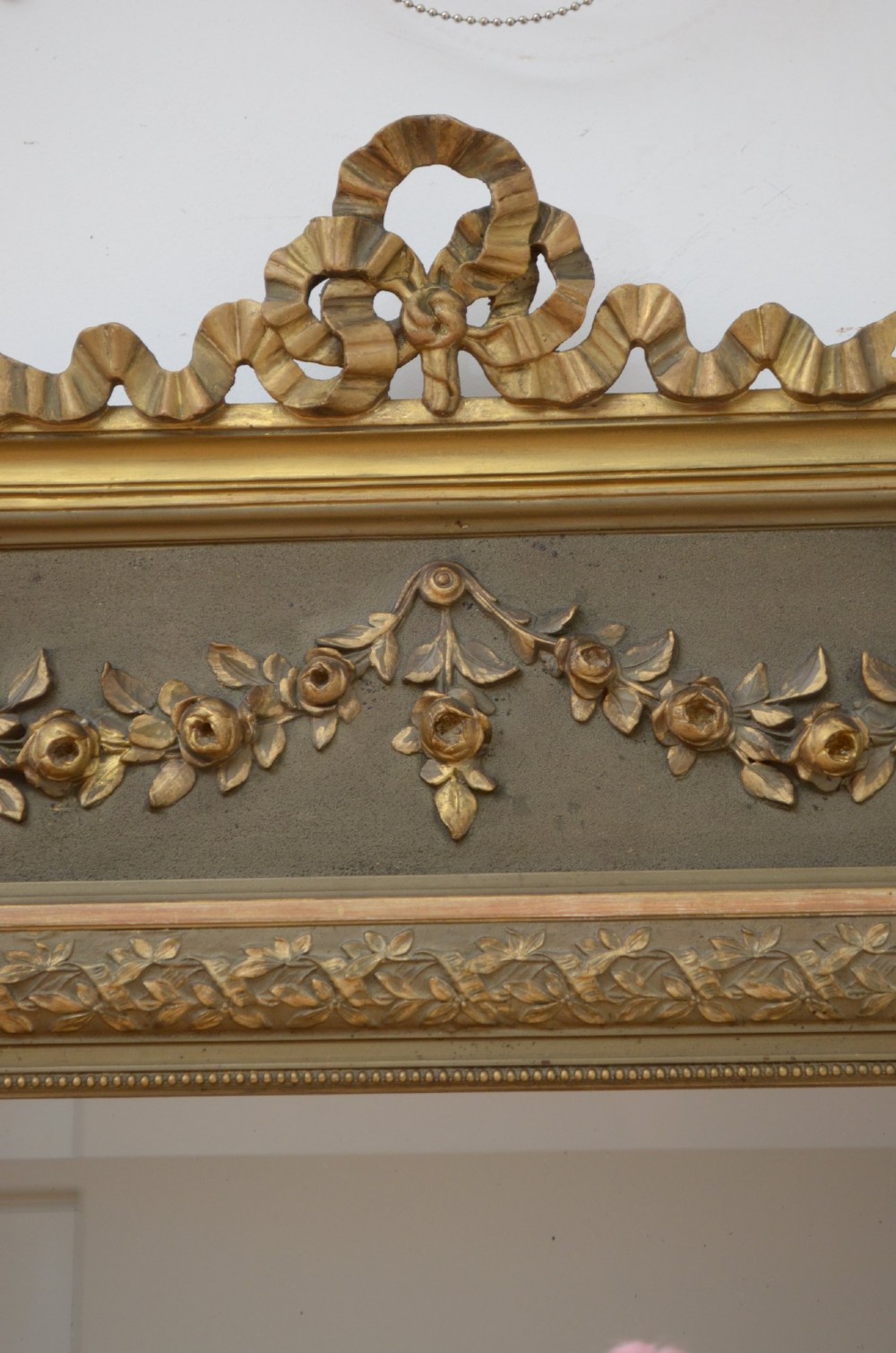 A tall antique French pier mirror featuring a gilded ribbon cresting, carved floral swags, and leaf moulding framing rectangular mirror glass. View III