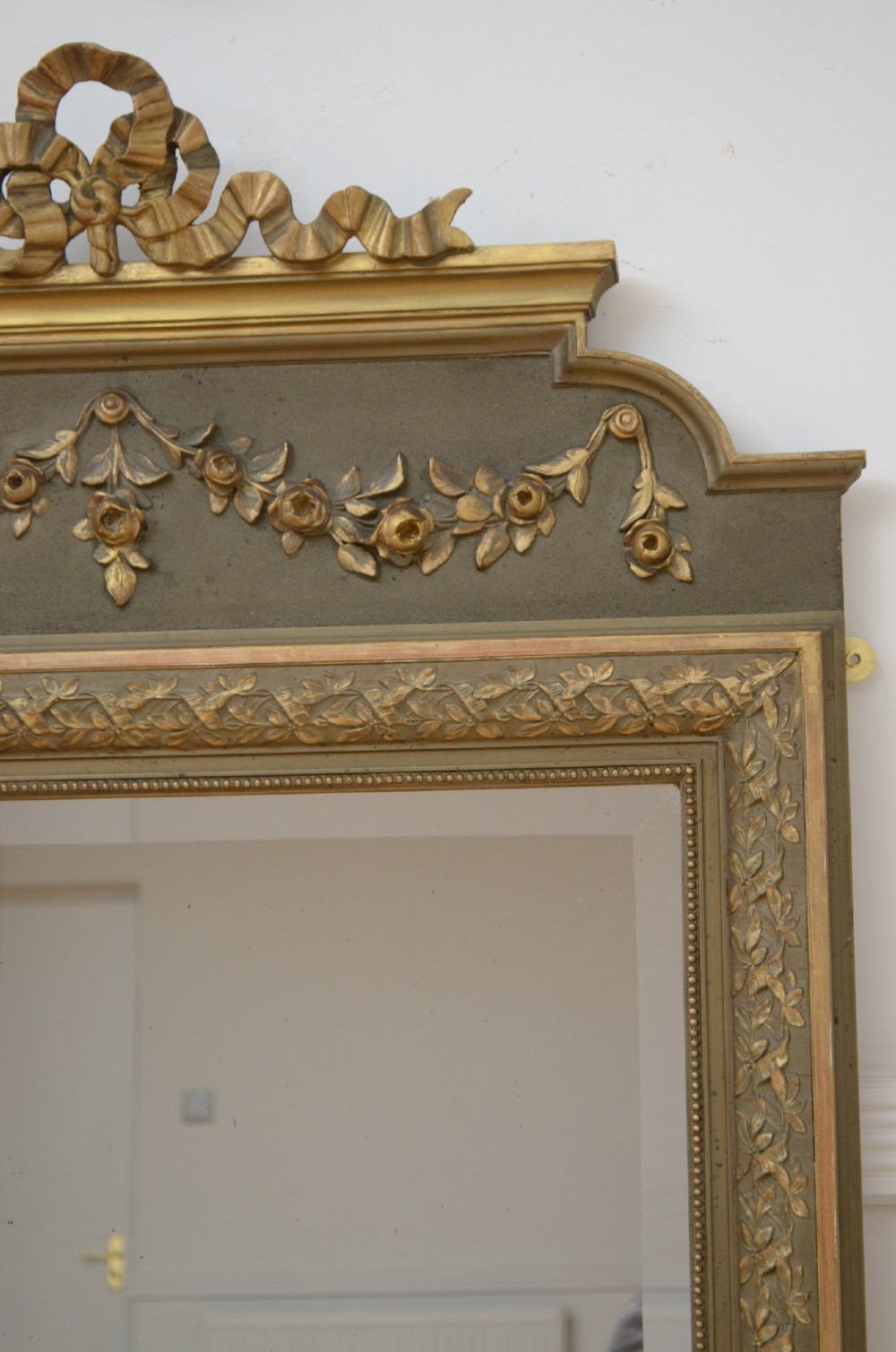 A tall antique French pier mirror featuring a gilded ribbon cresting, carved floral swags, and leaf moulding framing rectangular mirror glass. View IV
