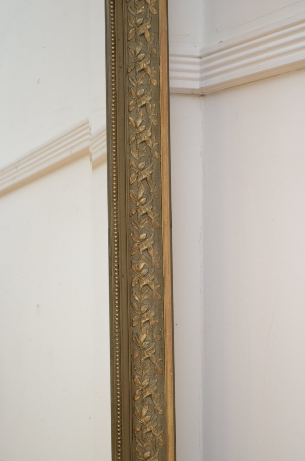 A tall antique French pier mirror featuring a gilded ribbon cresting, carved floral swags, and leaf moulding framing rectangular mirror glass. View V