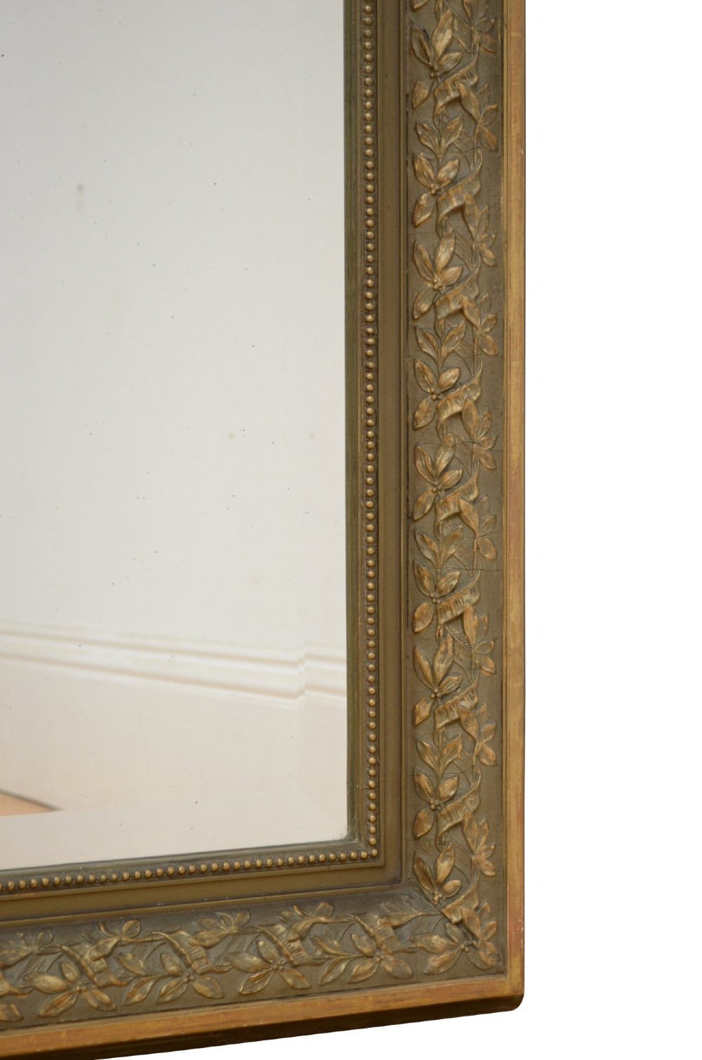 A tall antique French pier mirror featuring a gilded ribbon cresting, carved floral swags, and leaf moulding framing rectangular mirror glass. View VI