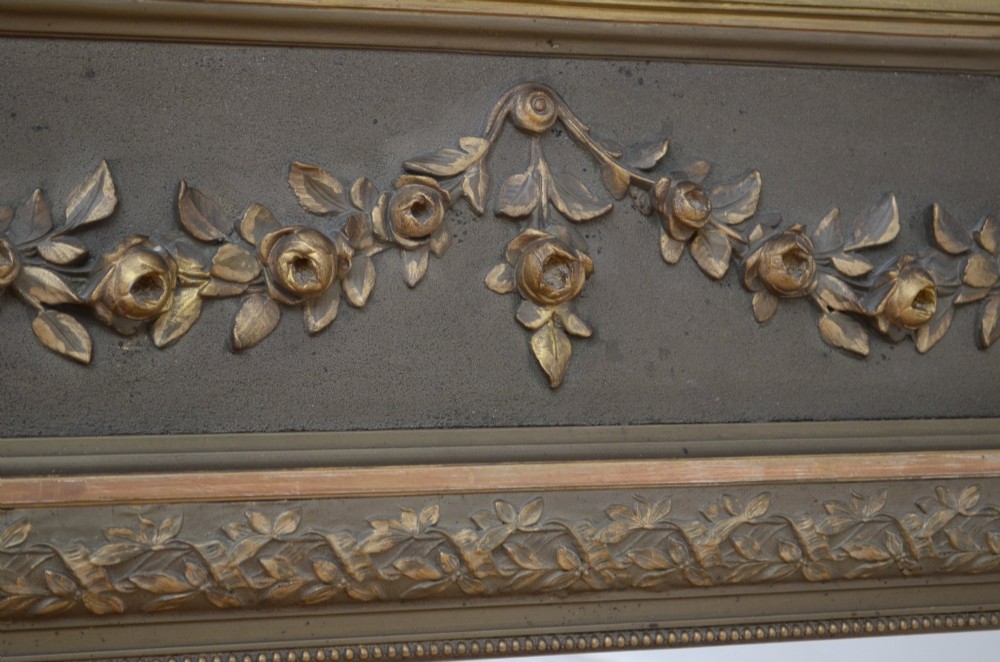 A tall antique French pier mirror featuring a gilded ribbon cresting, carved floral swags, and leaf moulding framing rectangular mirror glass. View VII