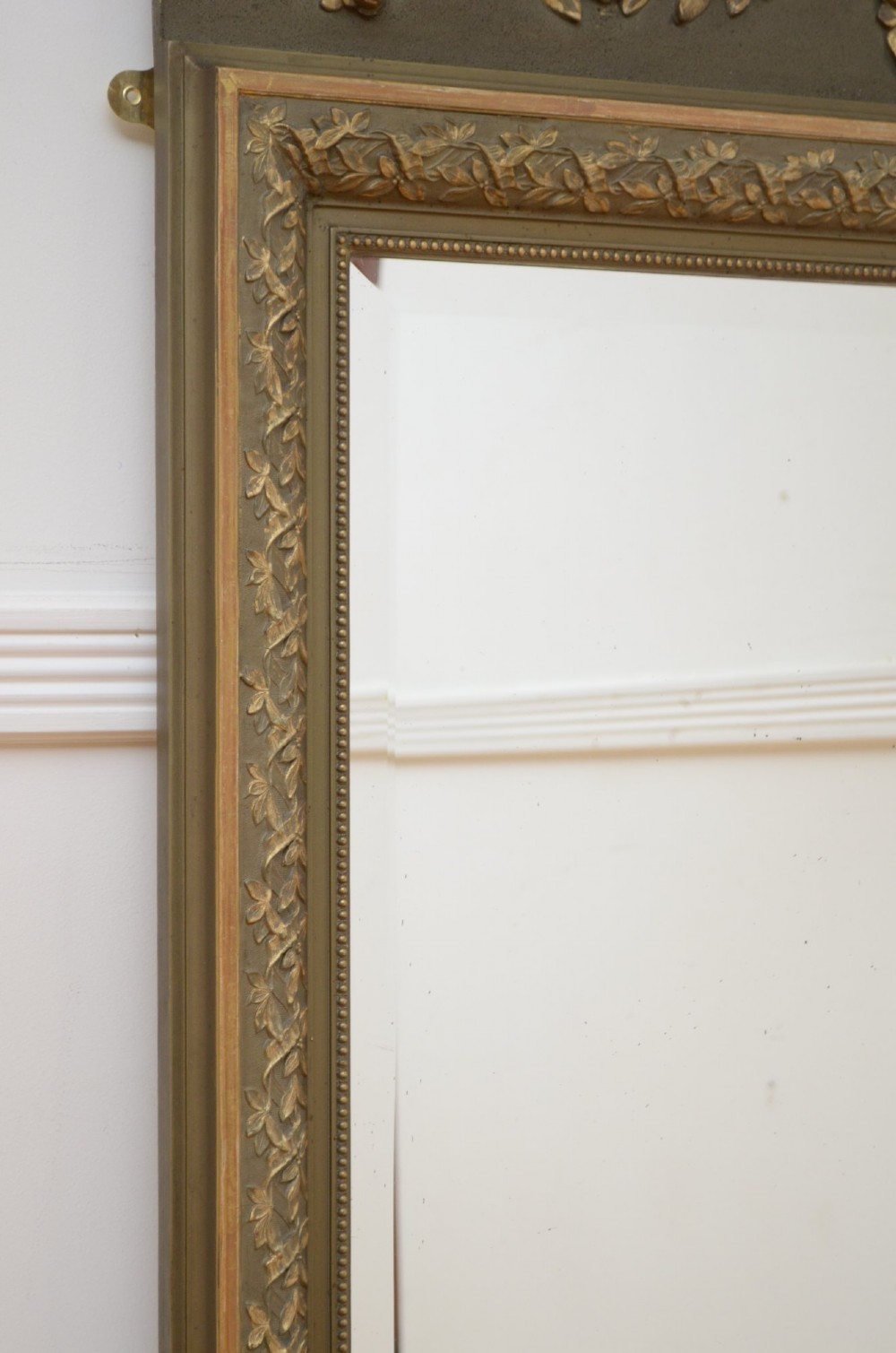 A tall antique French pier mirror featuring a gilded ribbon cresting, carved floral swags, and leaf moulding framing rectangular mirror glass. View XII