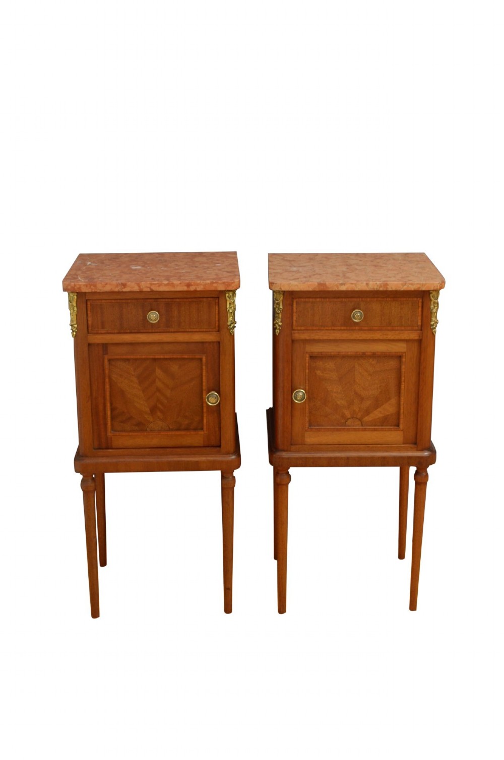 A pair of tall French Louis XVI style wooden bedside cabinets featuring pink marble tops, single drawers, cupboard doors with sunburst parquetry motifs, and slender turned legs.
