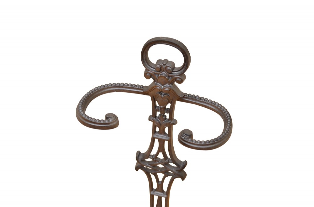A cast iron umbrella stand featuring a central decorative stem, two curved upper retaining arms, a top loop handle, and an oval drip tray base. View IV