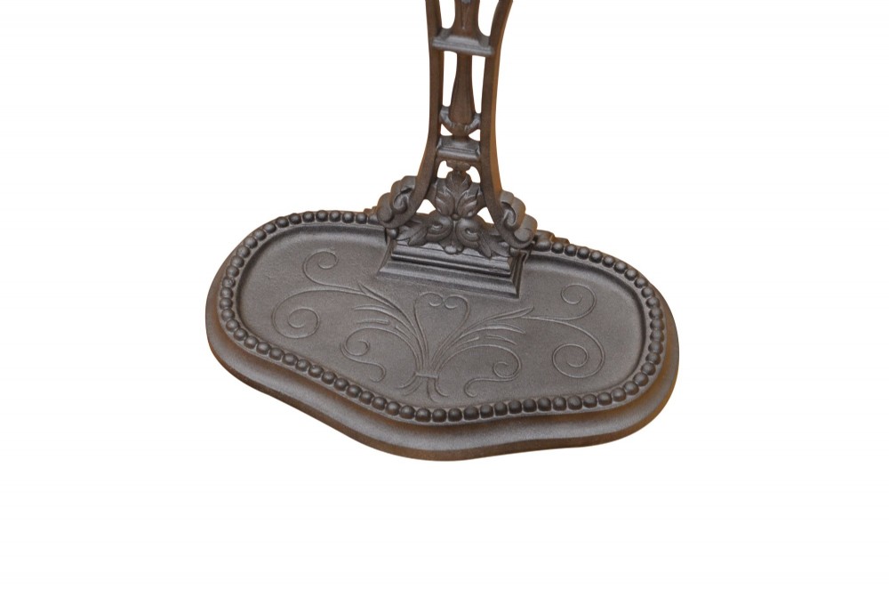 A cast iron umbrella stand featuring a central decorative stem, two curved upper retaining arms, a top loop handle, and an oval drip tray base. View IX
