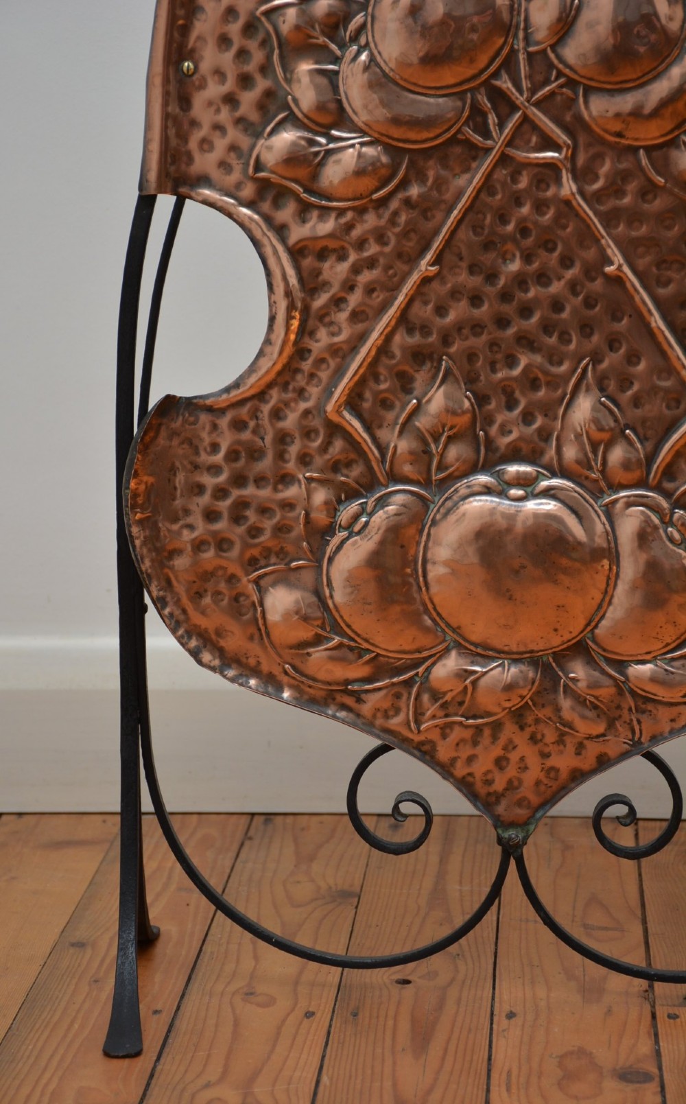 An Arts and Crafts fire screen featuring a shaped copper panel with hand-hammered botanical repousse work suspended inside a black wrought iron frame. View III