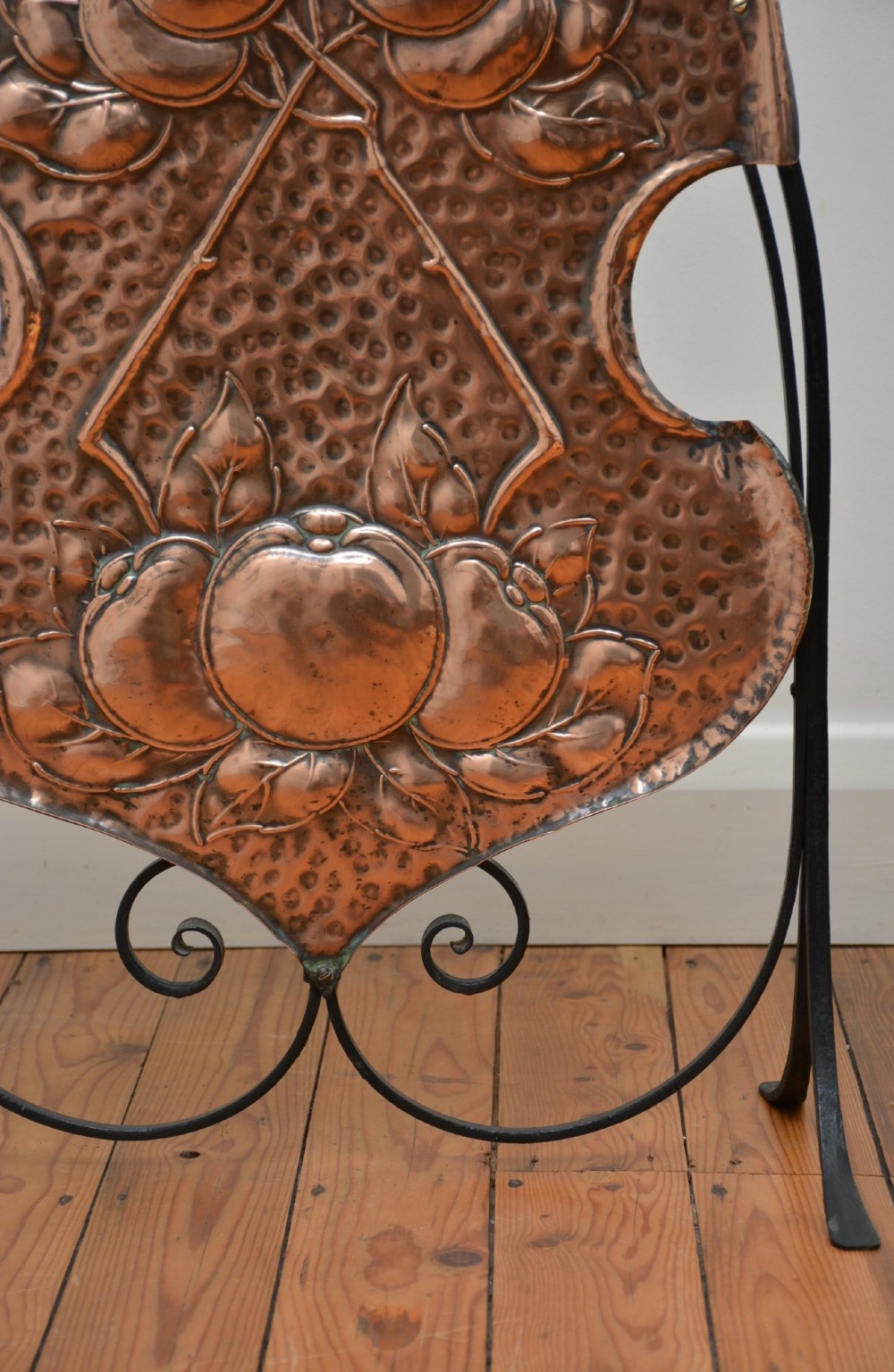 An Arts and Crafts fire screen featuring a shaped copper panel with hand-hammered botanical repousse work suspended inside a black wrought iron frame. View IV