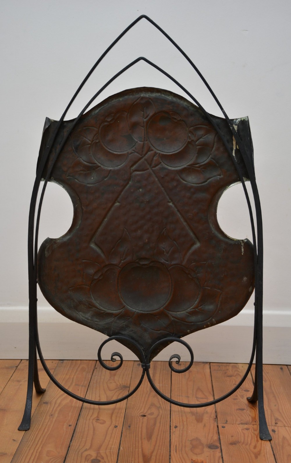 An Arts and Crafts fire screen featuring a shaped copper panel with hand-hammered botanical repousse work suspended inside a black wrought iron frame. View XI
