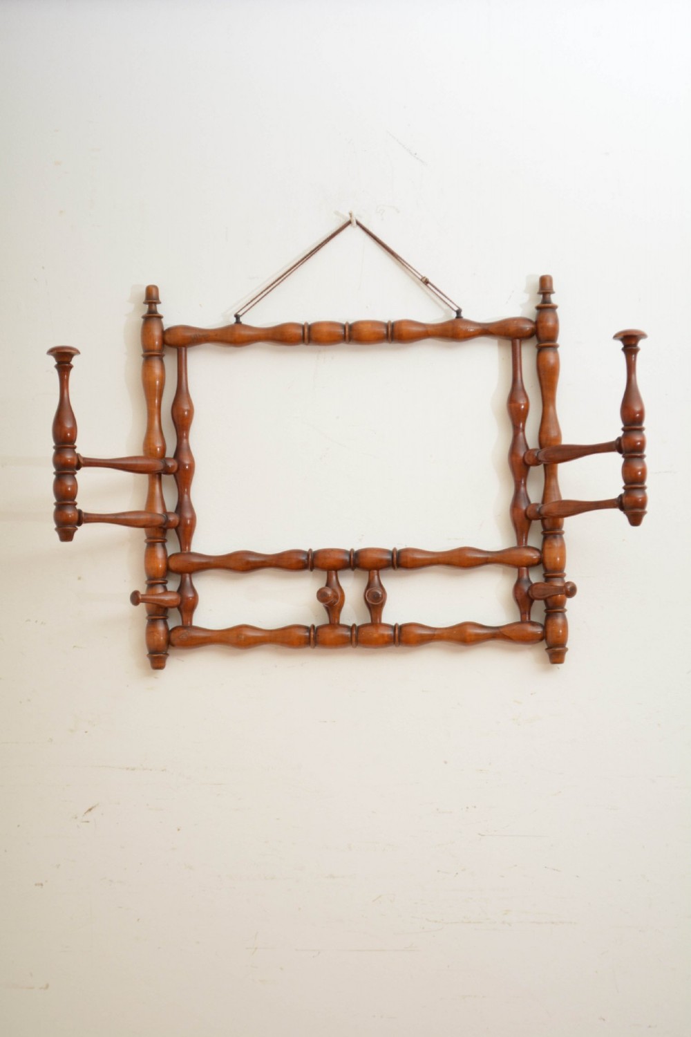 A wall-mounted coat rack made of turned warm brown wood spindles featuring multiple projecting hanging pegs and a top hanging cord. View IV