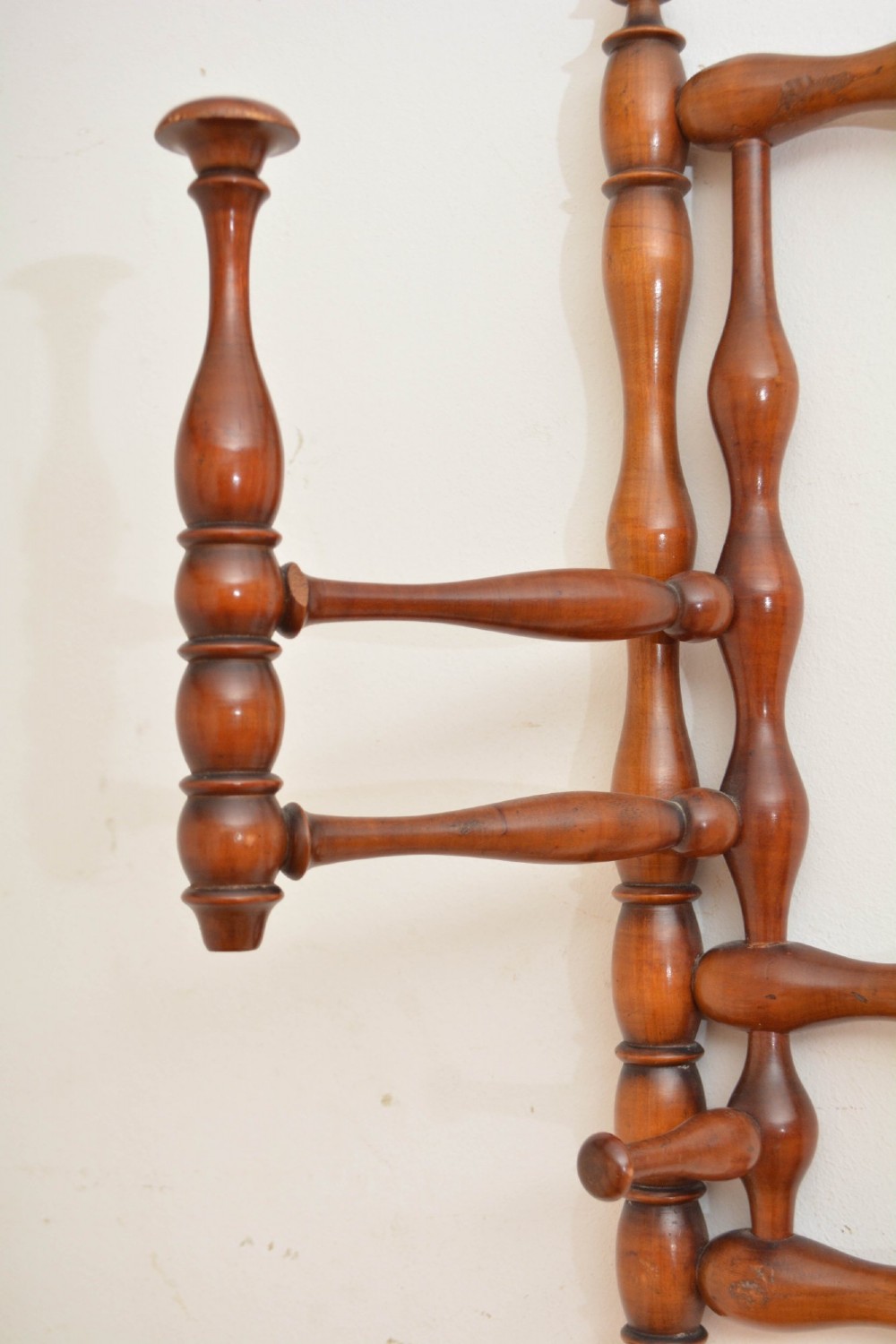 A wall-mounted coat rack made of turned warm brown wood spindles featuring multiple projecting hanging pegs and a top hanging cord. View VIII