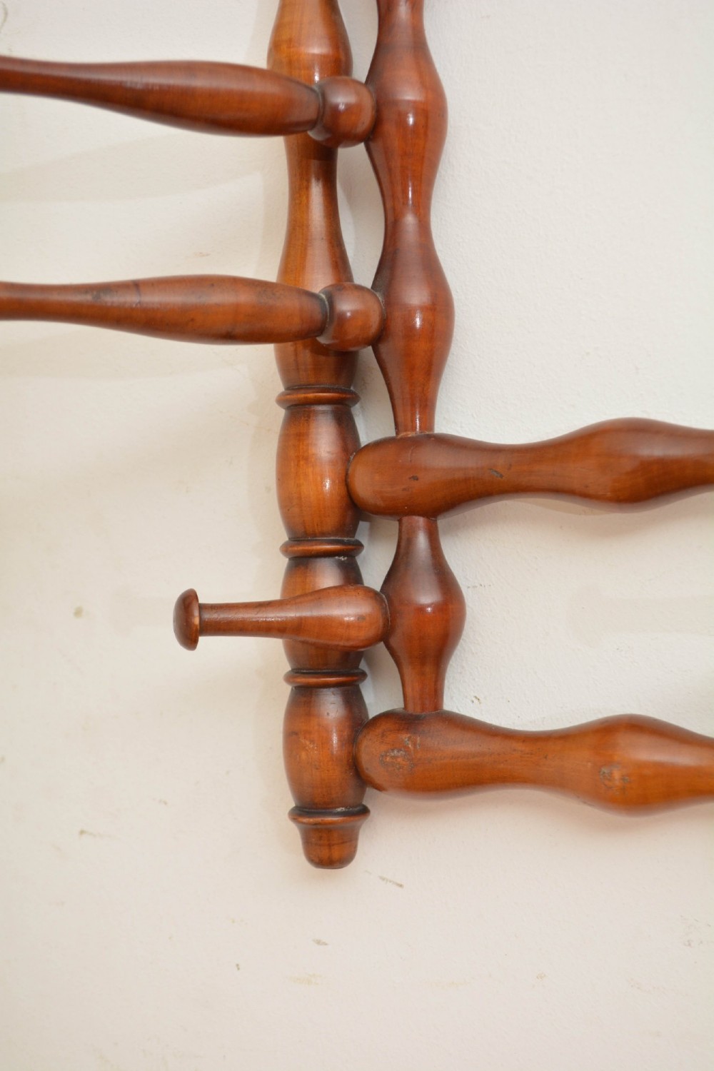 A wall-mounted coat rack made of turned warm brown wood spindles featuring multiple projecting hanging pegs and a top hanging cord. View IX