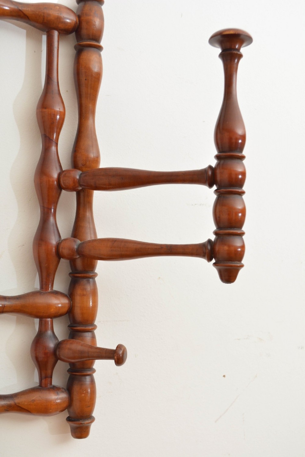 A wall-mounted coat rack made of turned warm brown wood spindles featuring multiple projecting hanging pegs and a top hanging cord. View XI