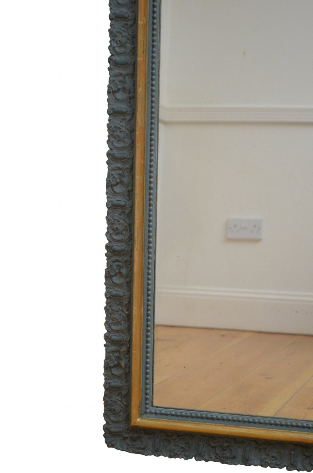 A tall rectangular wall mirror featuring a dark grey carved frame with a golden inner bead and an intricate foliage crest at the top. View VI