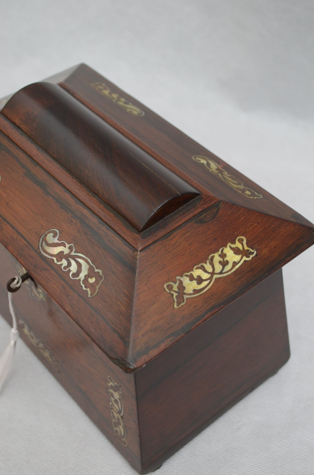 A Regency period rosewood tea caddy in a sarcophagus shape with mother-of-pearl floral scroll inlay and a brass keyhole. View IV
