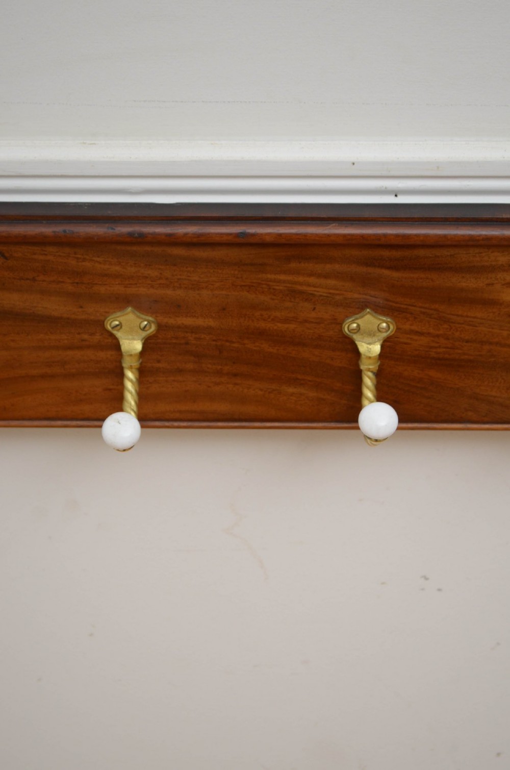 An antique wall-mounted mahogany coat rack featuring five rope-twist brass hooks topped with white ceramic knobs and carved scrollwork details. View VIII