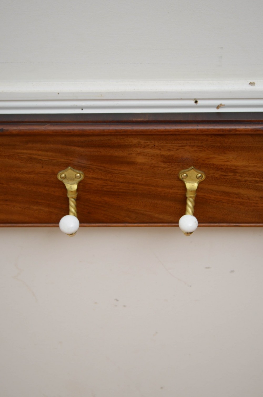 An antique wall-mounted mahogany coat rack featuring five rope-twist brass hooks topped with white ceramic knobs and carved scrollwork details. View IX