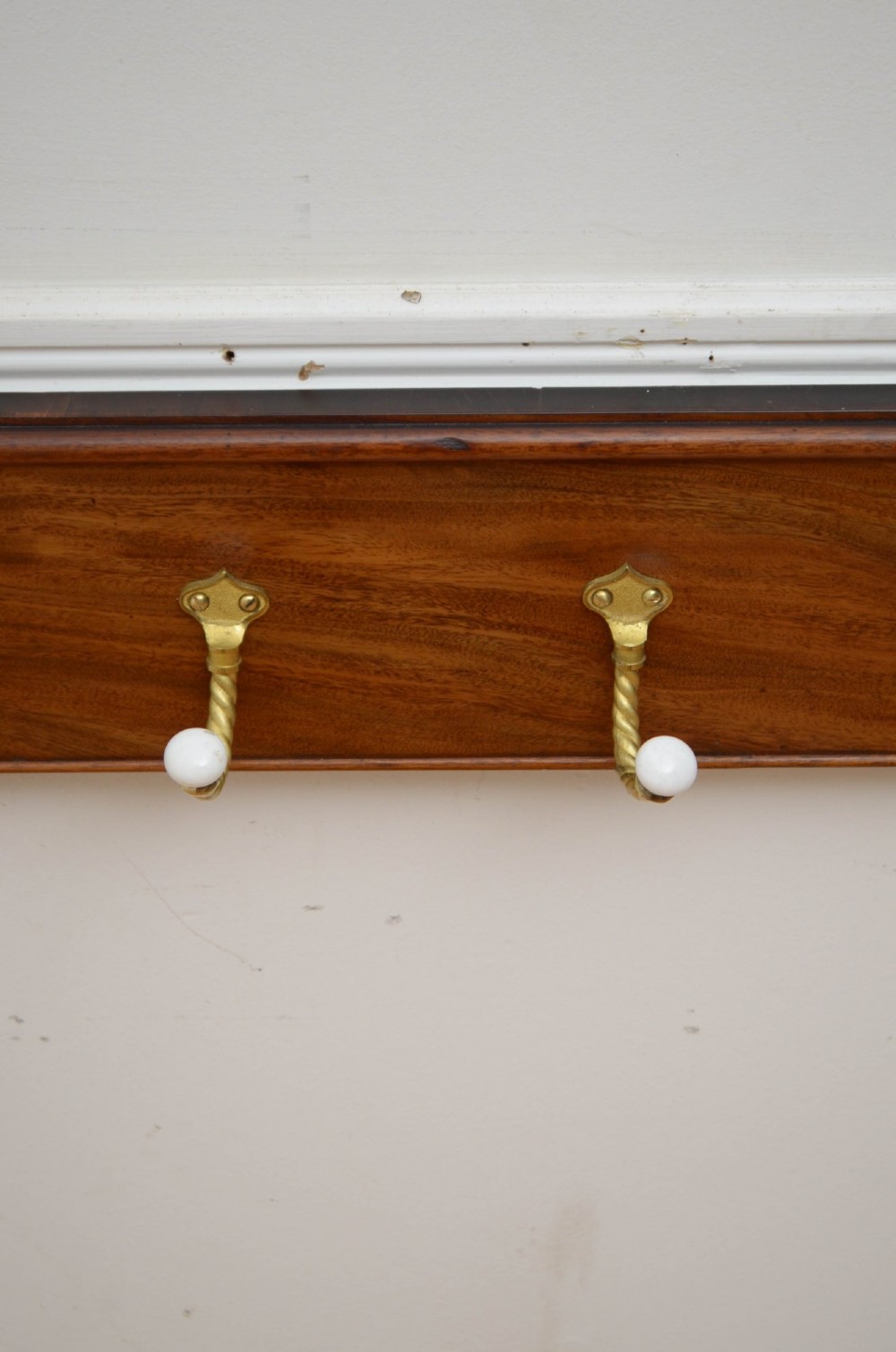 An antique wall-mounted mahogany coat rack featuring five rope-twist brass hooks topped with white ceramic knobs and carved scrollwork details. View X