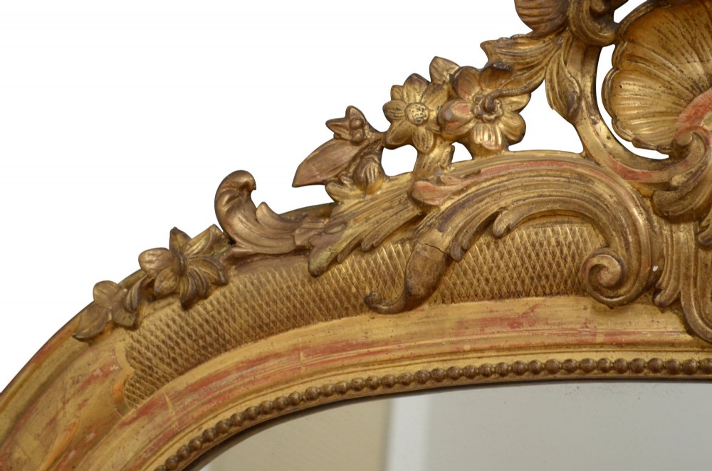 A tall arched giltwood wall mirror featuring an intricate shell cresting at the top and floral carved motifs along the gilded frame. View VII