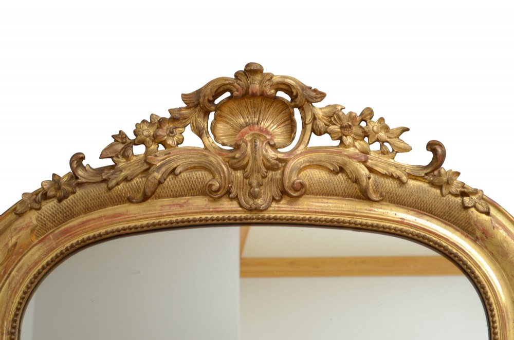 A tall arched giltwood wall mirror featuring an intricate shell cresting at the top and floral carved motifs along the gilded frame. View VIII
