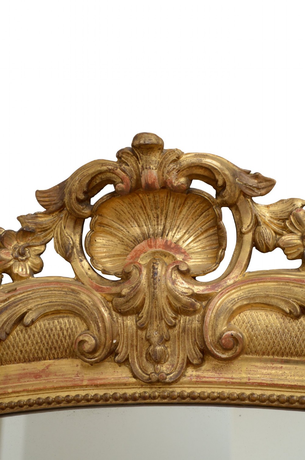 A tall arched giltwood wall mirror featuring an intricate shell cresting at the top and floral carved motifs along the gilded frame. View IX